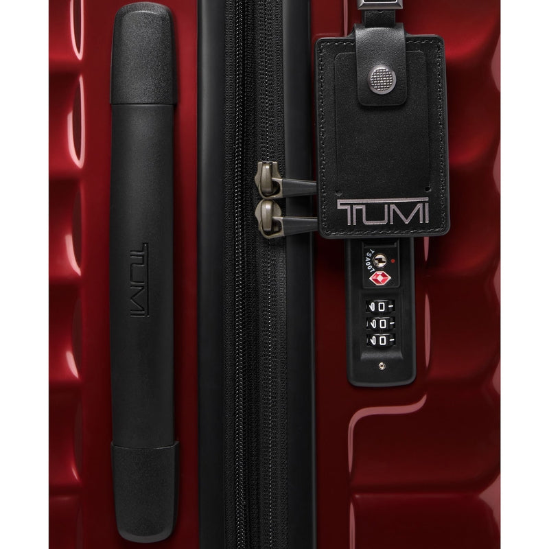 Red TUMI suitcase with black handle and tag on a red background