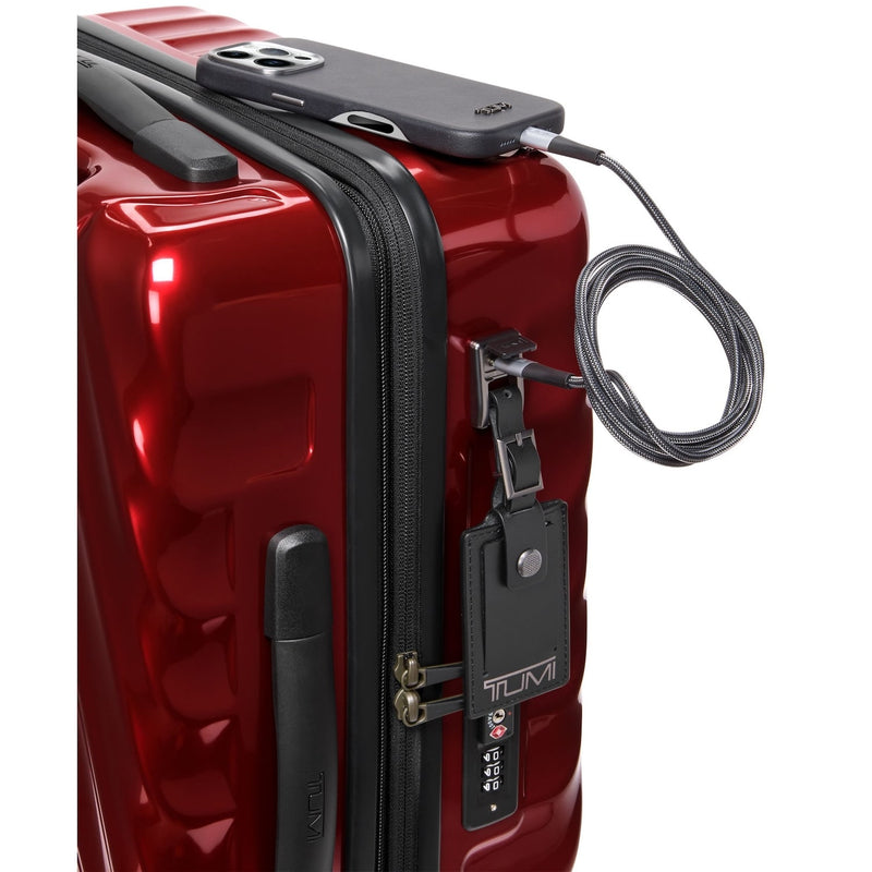 Red TUMI suitcase with a black phone, cable, and tag on a white background