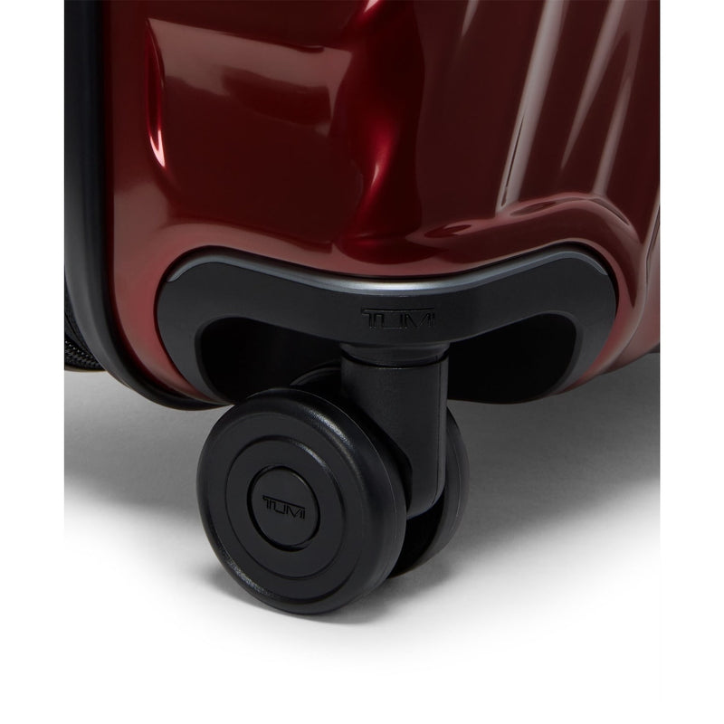 Close-up of a red TUMI suitcase with a black wheel on a white background