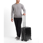 Person holding a black TUMI suitcase on a white background