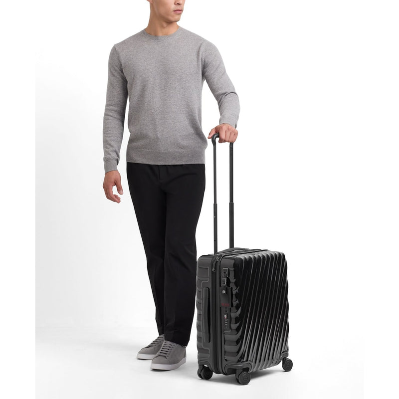 Person holding a black TUMI suitcase on a white background