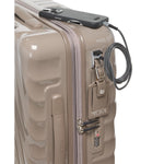 Beige TUMI suitcase with a black phone and cable on top, on a white background
