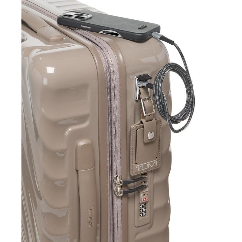 Beige TUMI suitcase with a black phone and cable on top, on a white background