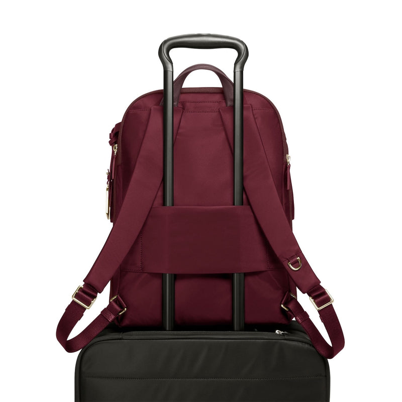 Maroon TUMI backpack with black rolling suitcase on a white background