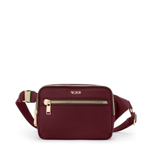 Wine TUMI crossbody bag with gold zippers on a white background