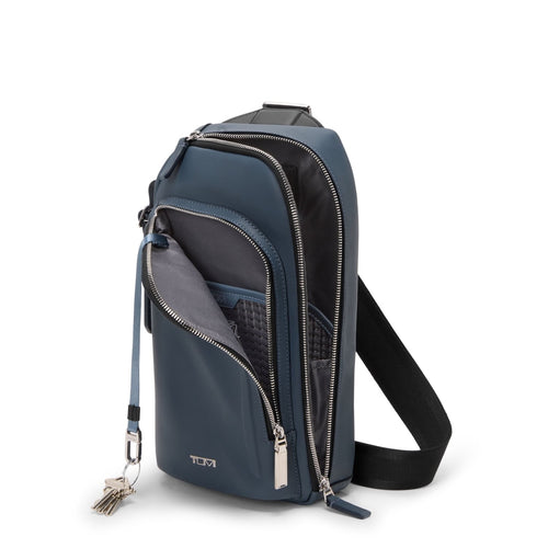 Blue TUMI sling bag with multiple zippers on a white background
