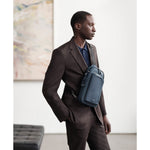 Man in a brown suit with a blue TUMI crossbody bag in an indoor setting