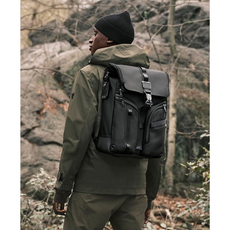 Person wearing a black TUMI backpack in a forest setting