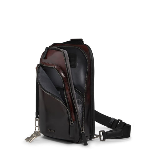 Black and brown TUMI sling bag with multiple zippers on a white background