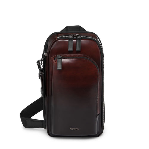 Brown leather TUMI crossbody bag with black accents on a white background