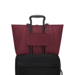 Wine TUMI tote bag on top of a black suitcase on a white background