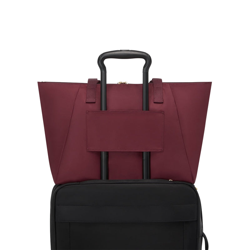 Wine TUMI tote bag on top of a black suitcase on a white background