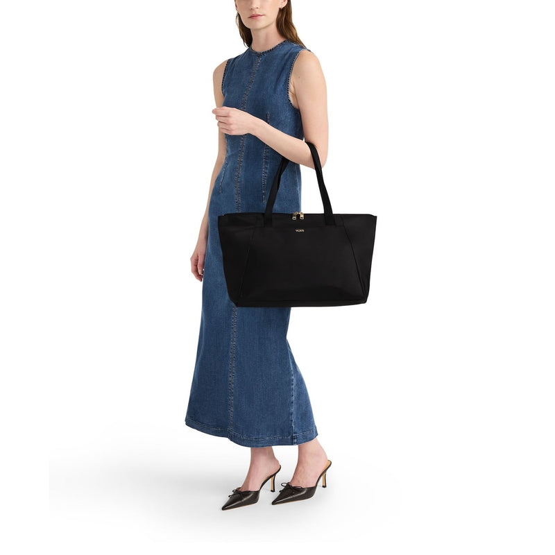 Woman holding a black TUMI tote bag against a white background