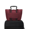 Wine TUMI tote bag with black handle on top of a black suitcase against a white background
