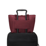 Wine TUMI tote bag with black handle on top of a black suitcase against a white background