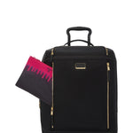 Black TUMI suitcase with gold accents and a pink and black pouch on a white background