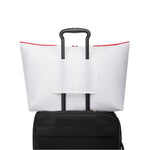 White TUMI tote bag with red accents on top of a black suitcase