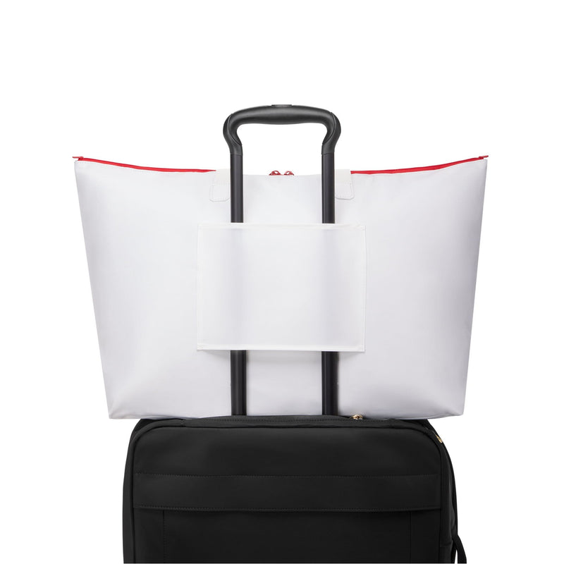 White TUMI tote bag with red accents on top of a black suitcase