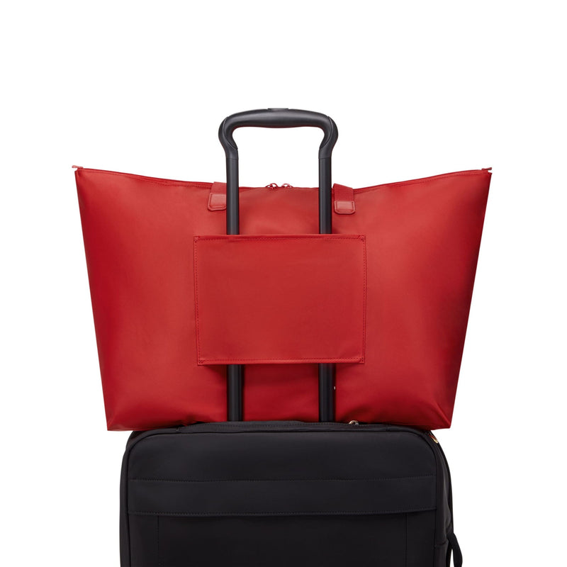 Red TUMI tote bag on top of a black suitcase on a white background