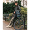 Man with a blue TUMI backpack sitting on a bicycle in a park setting