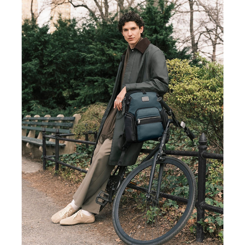 Man with a blue TUMI backpack sitting on a bicycle in a park setting