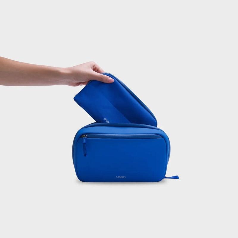 Blue orbitkey travel pouch being held by a hand on a light gray background