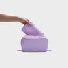 Purple orbitkey travel bag with a hand lifting the inner pouch on a light gray background