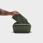 Green orbitkey travel toiletry bag with a hand opening it on a light gray background