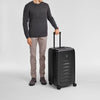Man holding a black Victorinox suitcase on a light gray background