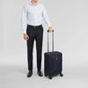 Man in formal attire holding a navy Victorinox suitcase on a light gray background