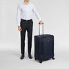 Man in white shirt and black pants holding a navy suitcase Victorinox on a light gray background
