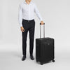 Person in formal attire holding a black Victorinox suitcase on a light gray background