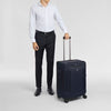 Person in formal attire holding a navy Victorinox suitcase on a light gray background