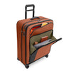 orange Briggs & Riley suitcase with front pockets loaded on a white background