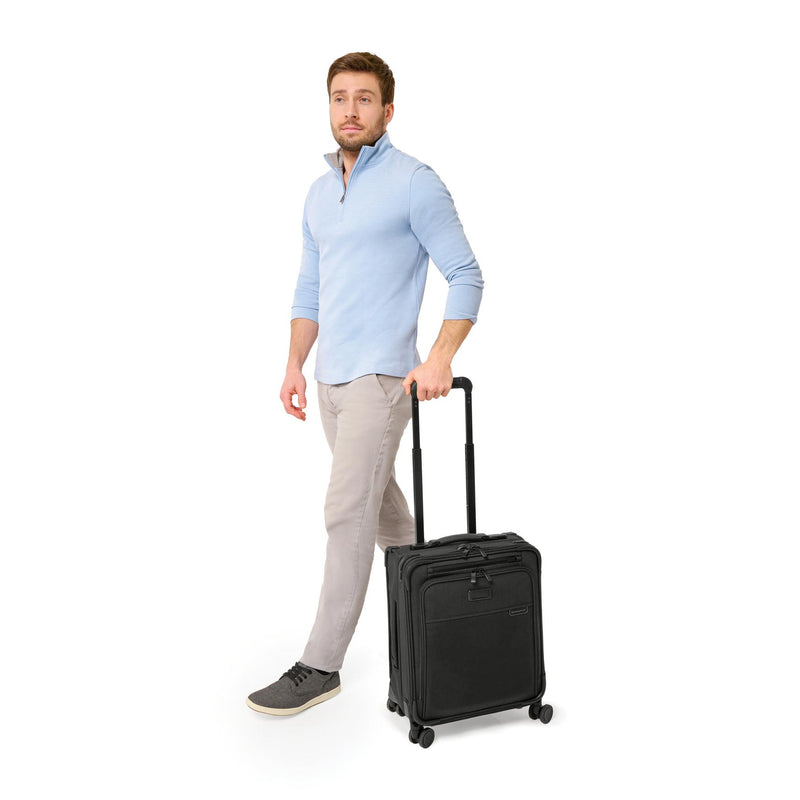 Model with black Briggs & Riley Baseline Compact Carry-On Spinner